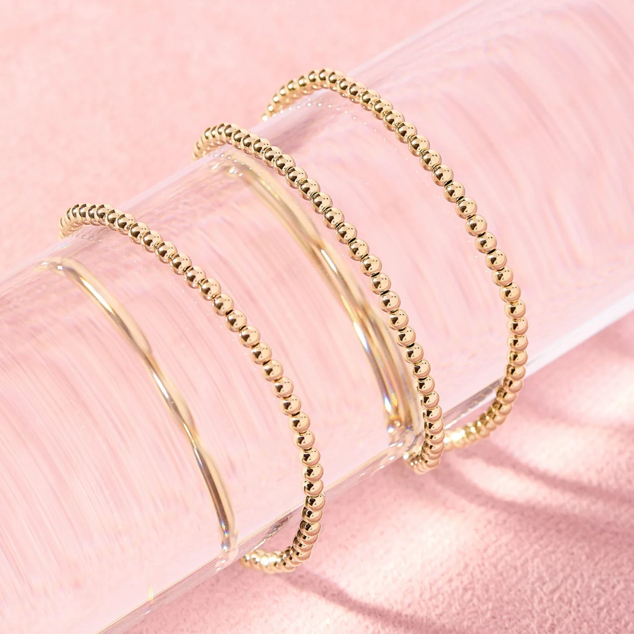Three gold beaded bracelets on a pink satin background