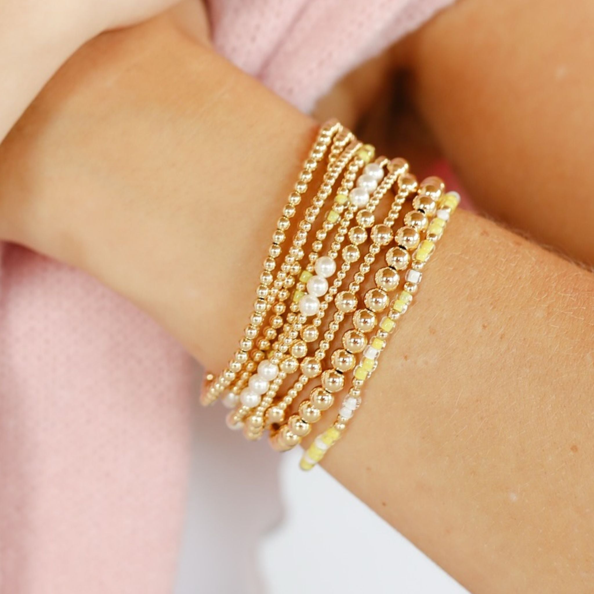 Close-up of a wrist wearing multiple gold and pearl beaded bracelets.