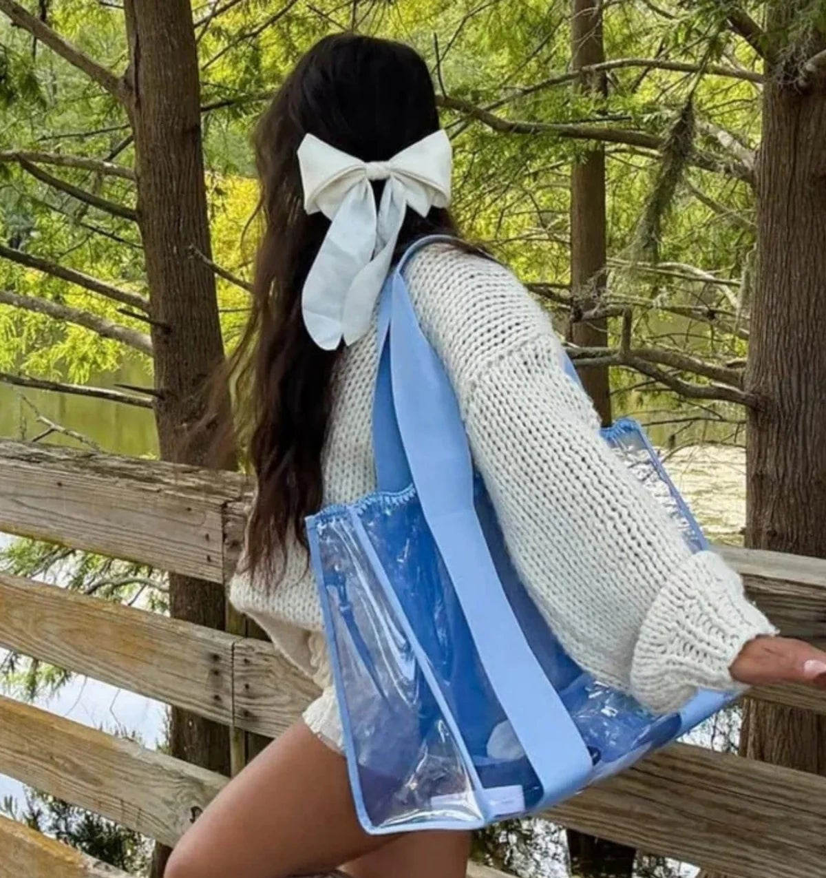 Person holding a blue and clear tote bag outdoors with trees in the background