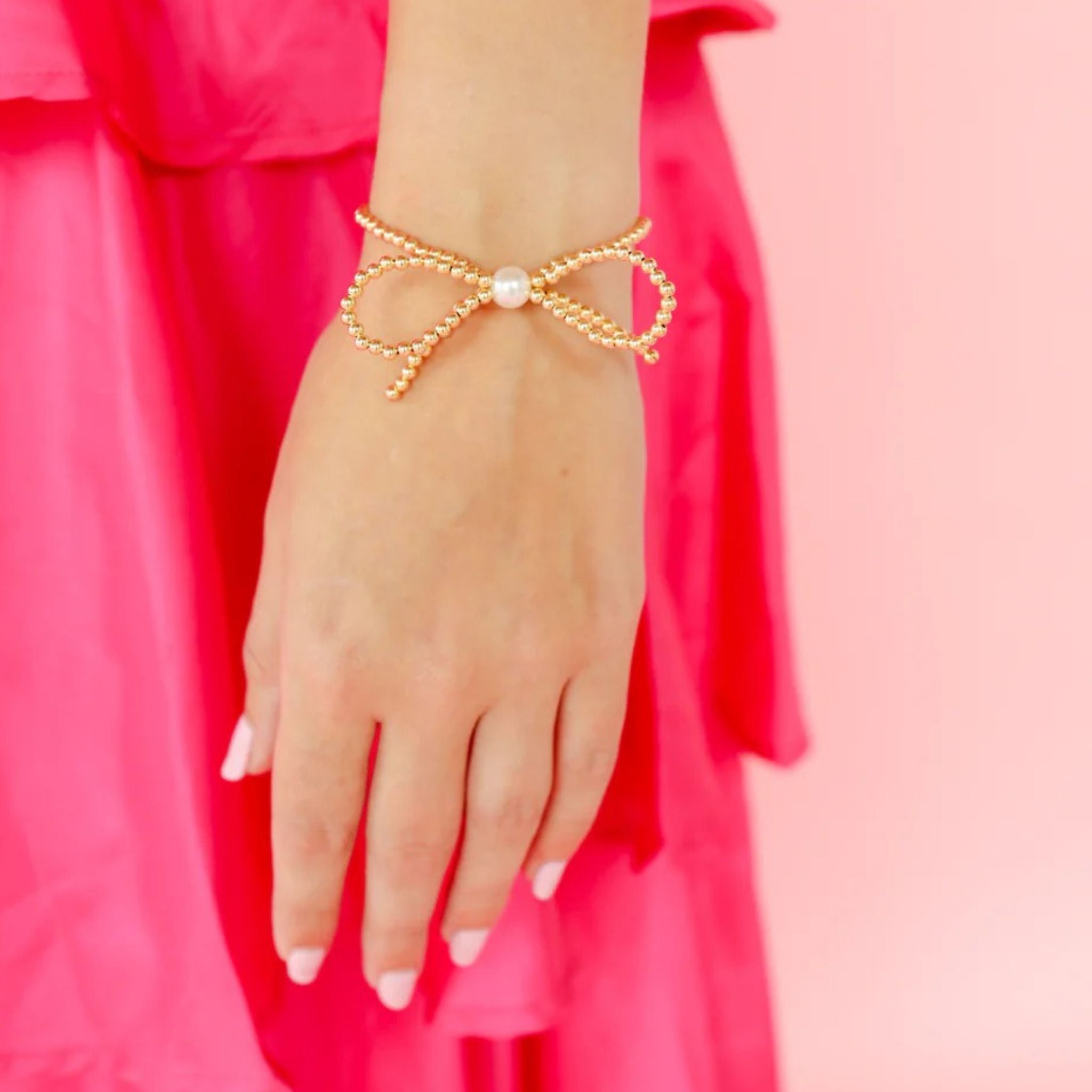 Gold bow-shaped bracelet on a hand with a pink background