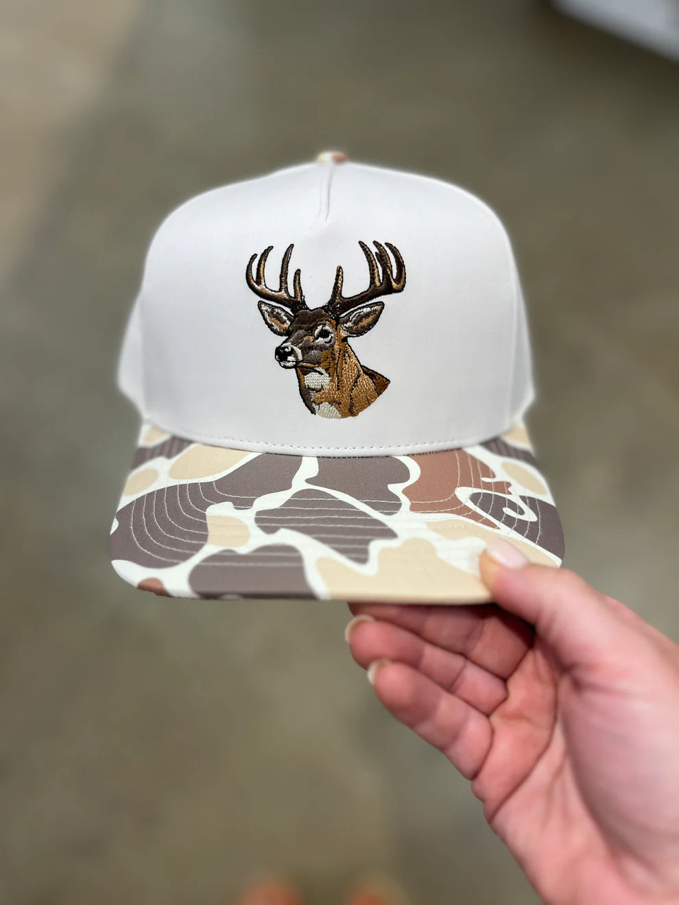 Cap with deer design and camouflage pattern held by a hand against a blurred background