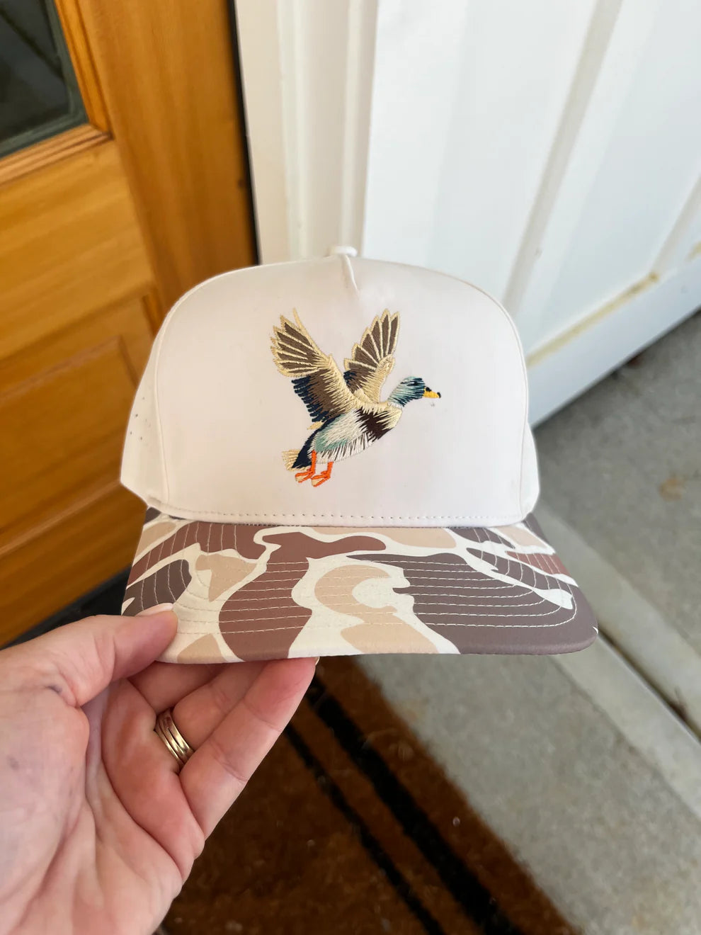 Cap with a bird design on a camouflage pattern held by a hand.