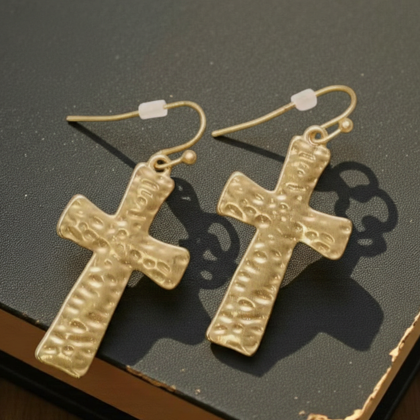 Gold cross earrings on a textured surface