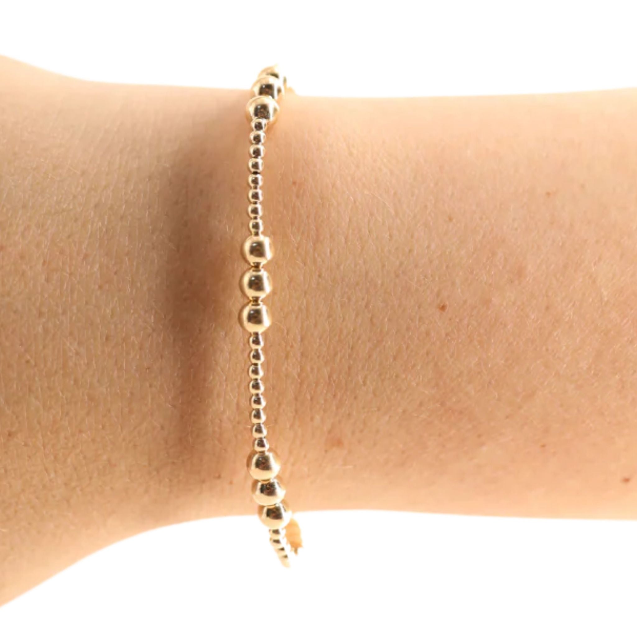 Gold beaded bracelet on a wrist against a white background