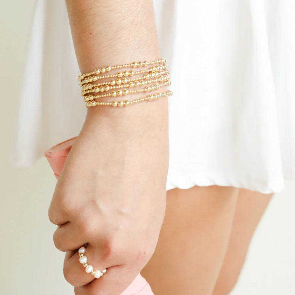 Hand wearing multiple gold bracelets on a plain background