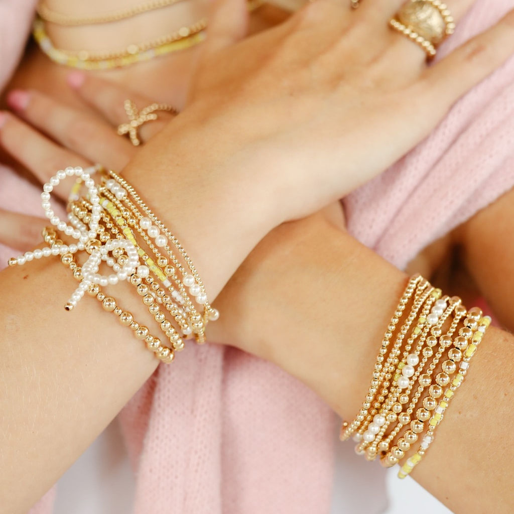 Close-up of hands wearing multiple gold bracelets on a light pink background