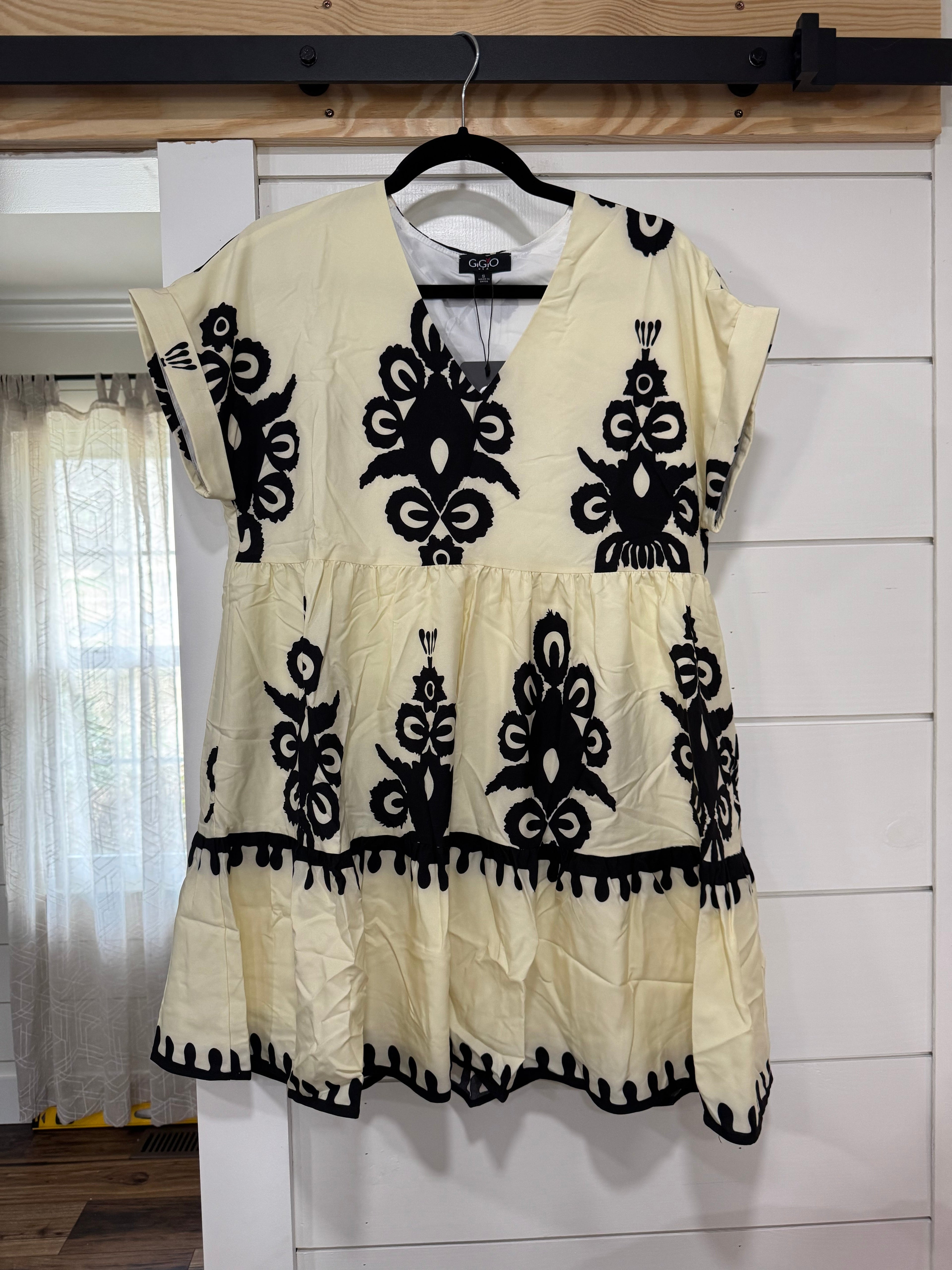 Beige dress with black embroidery on a hanger against a white wall.