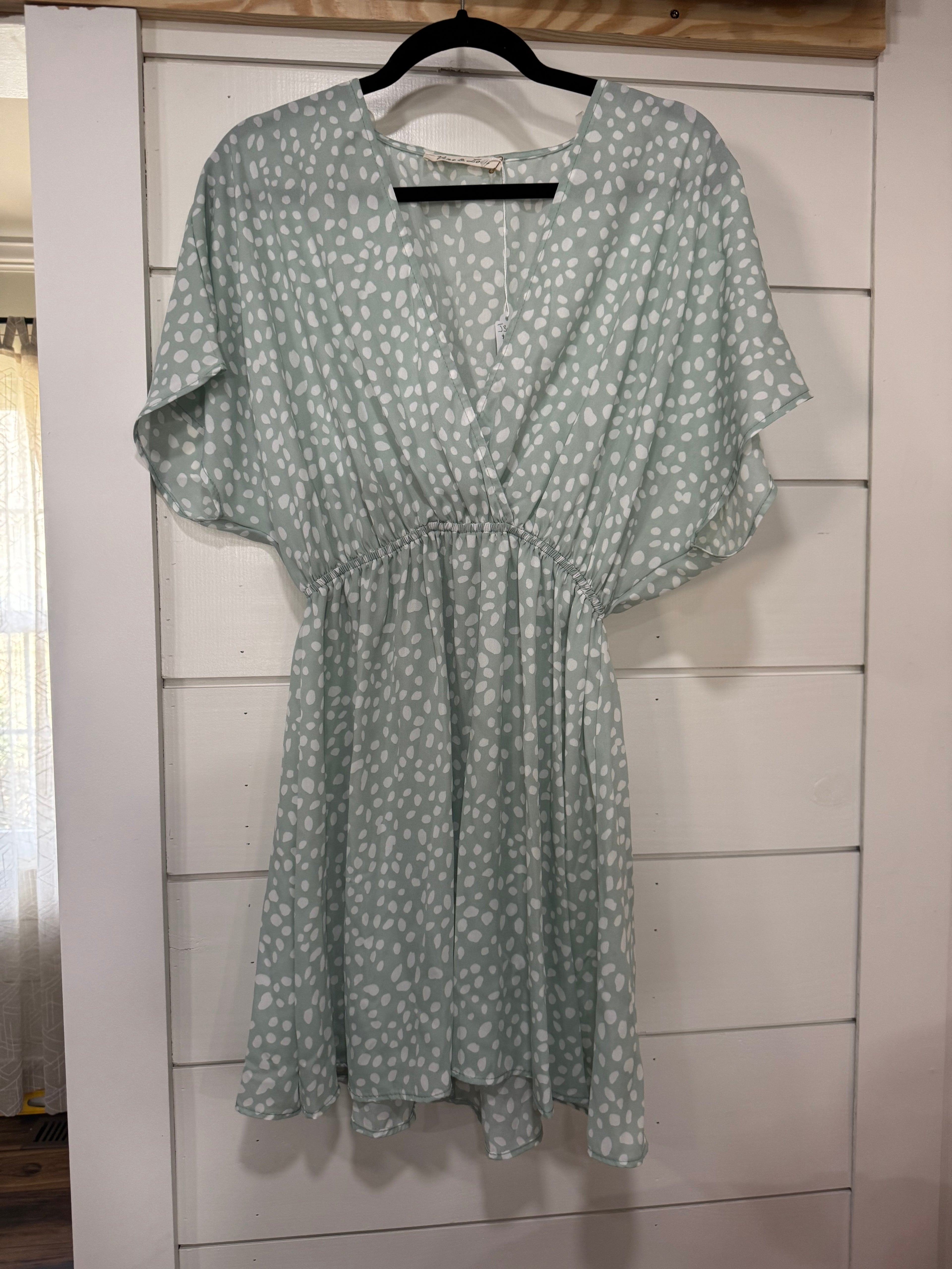 Green dress with white floral pattern hanging on a wooden rack.