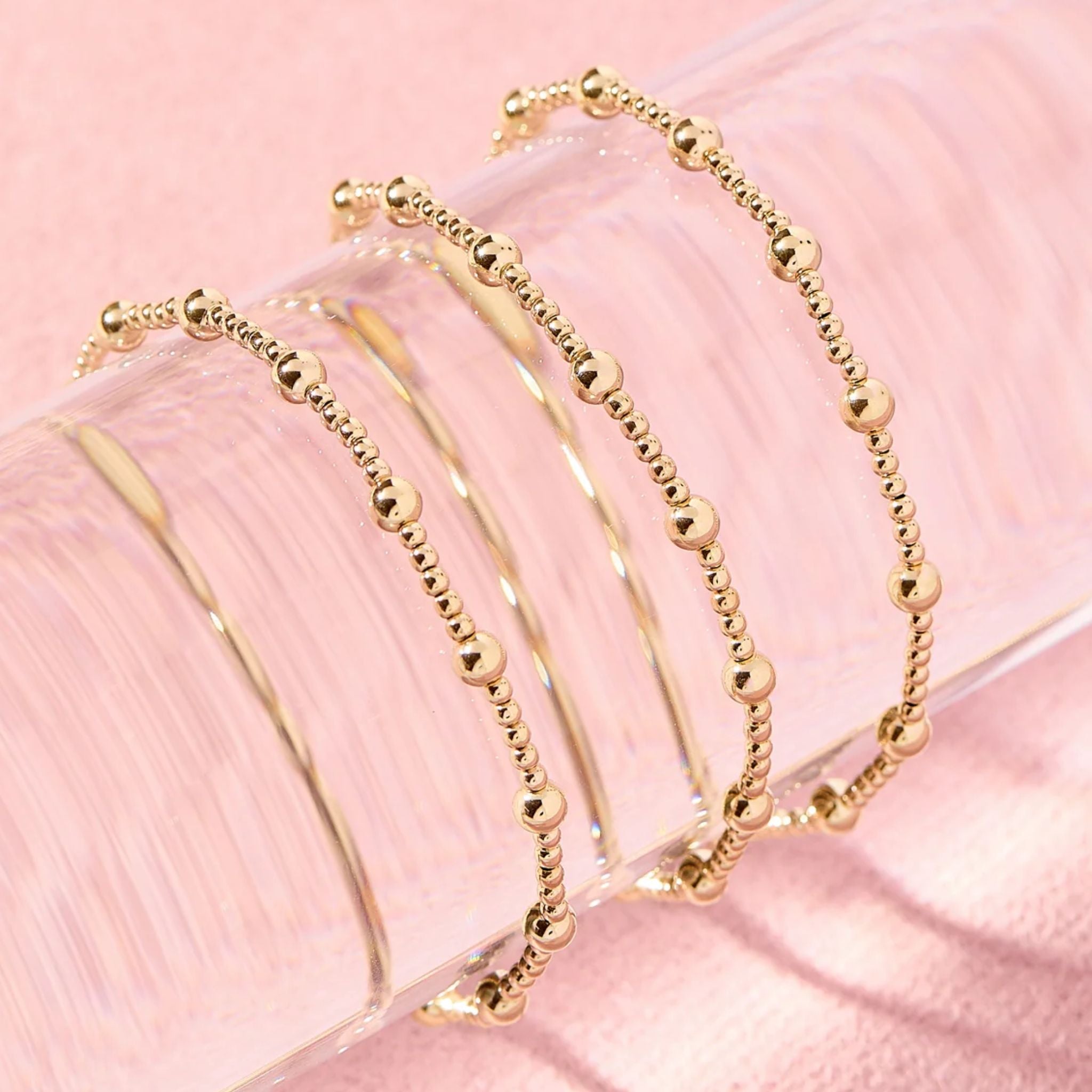 Gold beaded bracelets on a pink surface