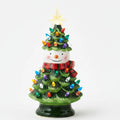 Three small ceramic Christmas tree figurines on a light gray background: one with a snowman head, one with a Santa Claus face in the middle, and one with a Santa Claus face on the right. The trees are green with multicolored lights and gold star toppers.
