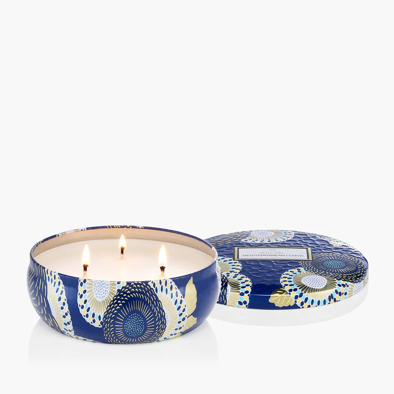 Decorative candle in a blue and white patterned tin with lid on a white background