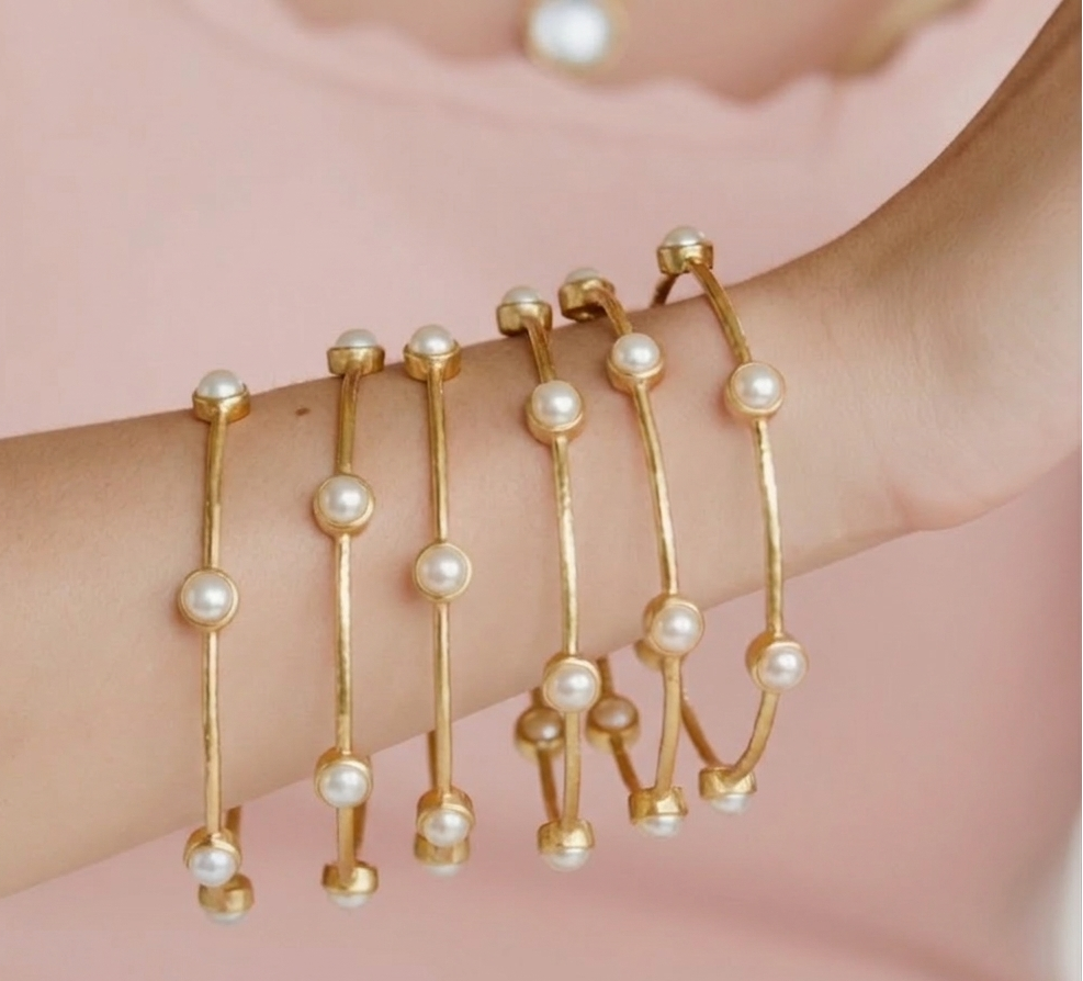 Gold bracelets with pearls on a wrist against a pink background