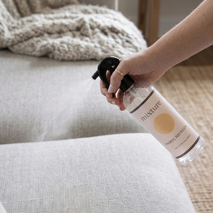 Person using a cleaning spray bottle on a sofa in a living room.