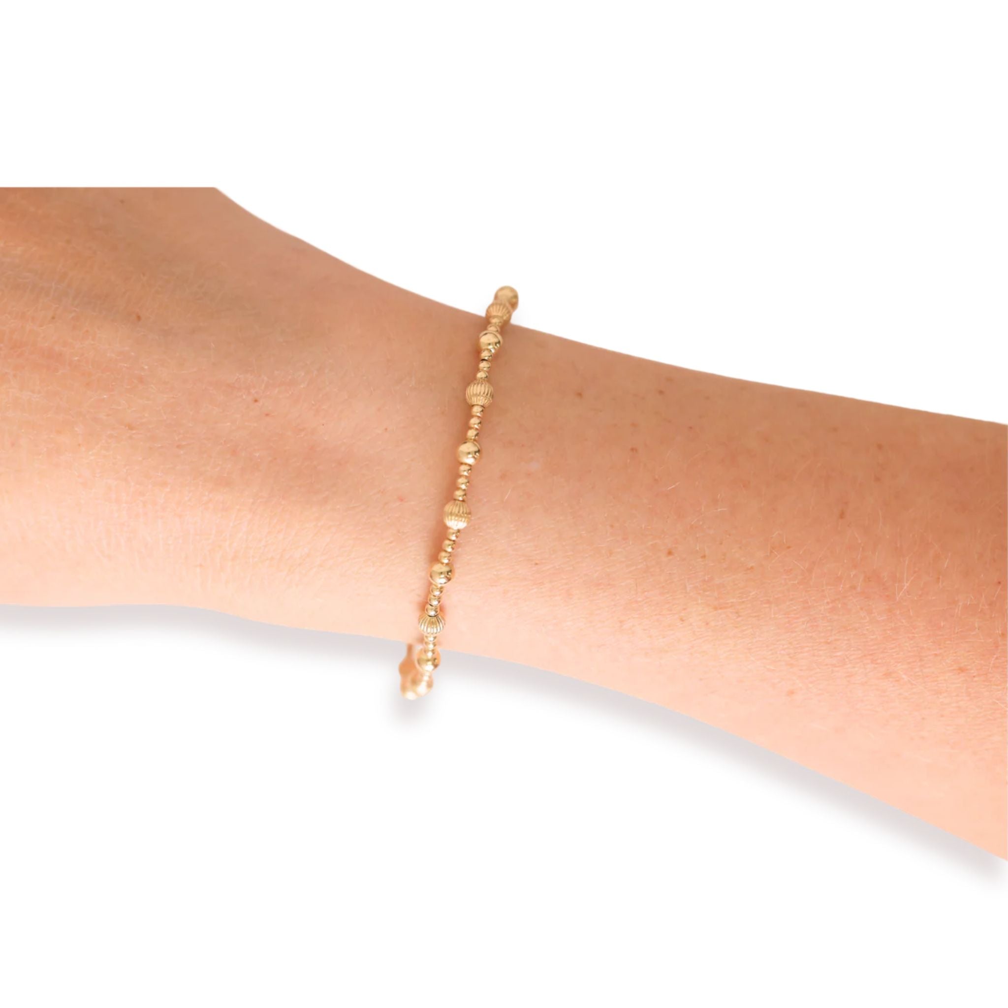 Gold beaded bracelet on a wrist against a white background