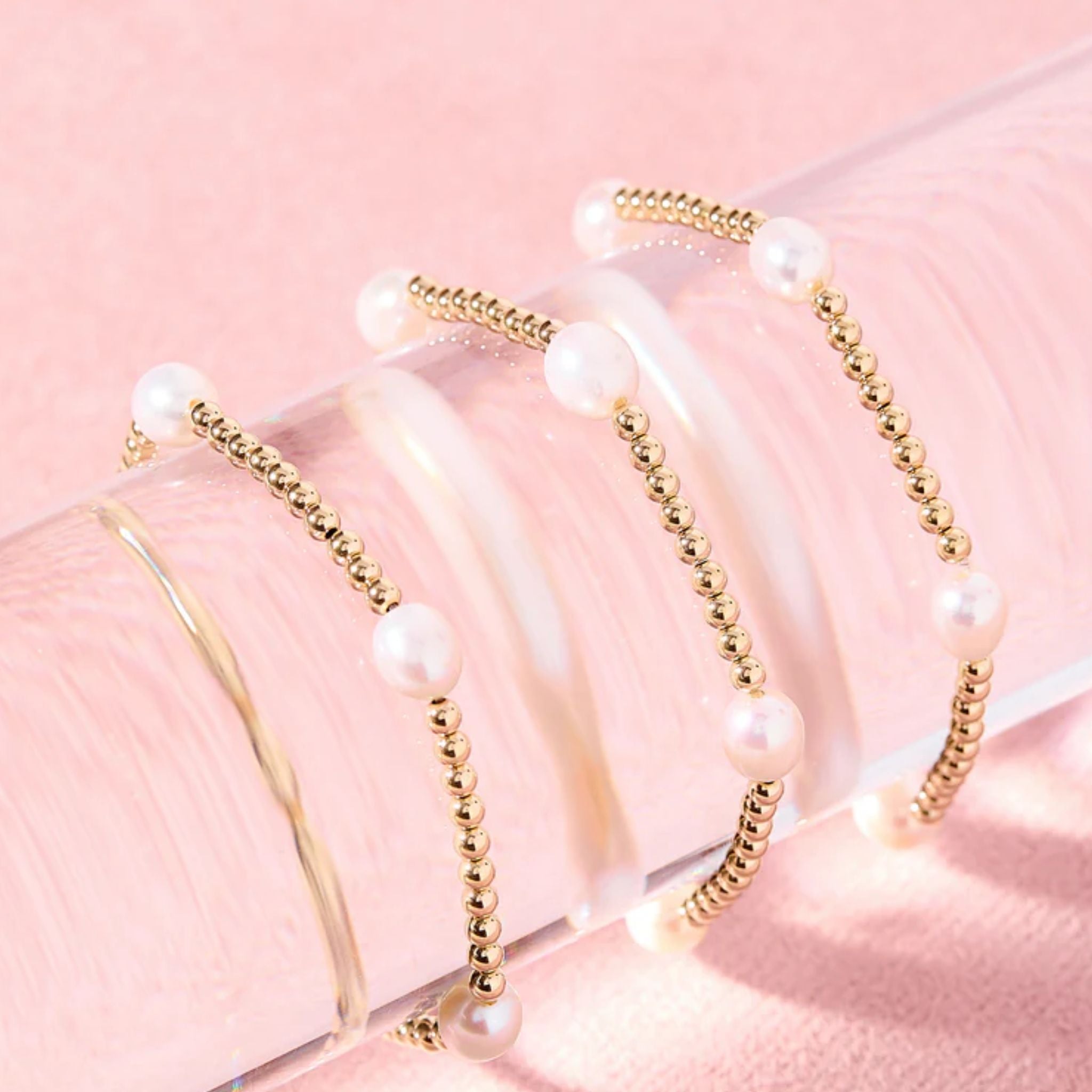 Set of pearl and gold beaded hairbands on a pink background