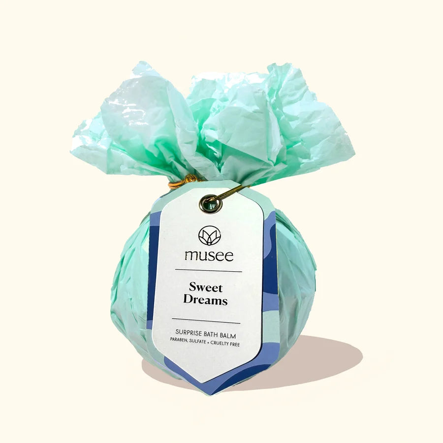 A wrapped bath balm package labeled 'musee Sweet Dreams' tied with crumpled mint green tissue paper, shown on a plain warm beige background.