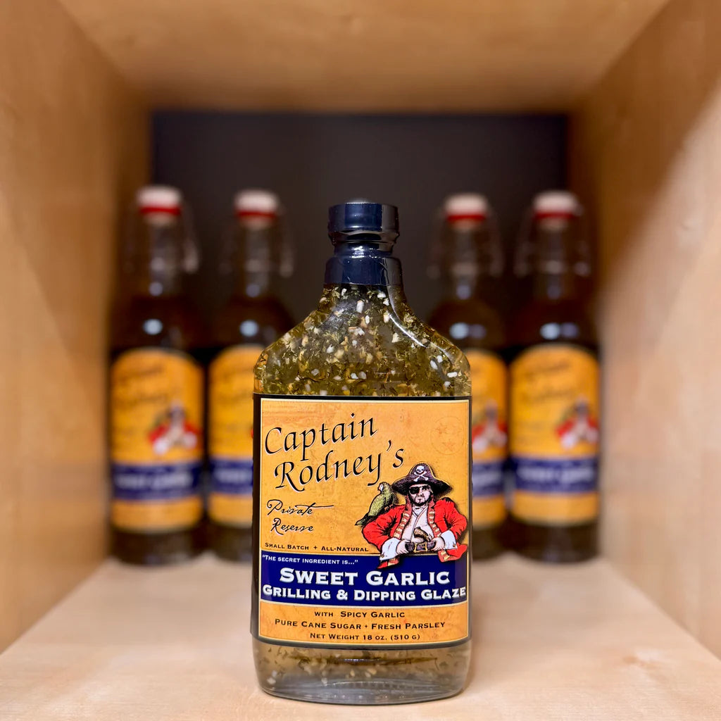 Bottle of Captain Rodney's Sweet Garlic Grilling & Dipping Glaze on a shelf with other similar bottles.