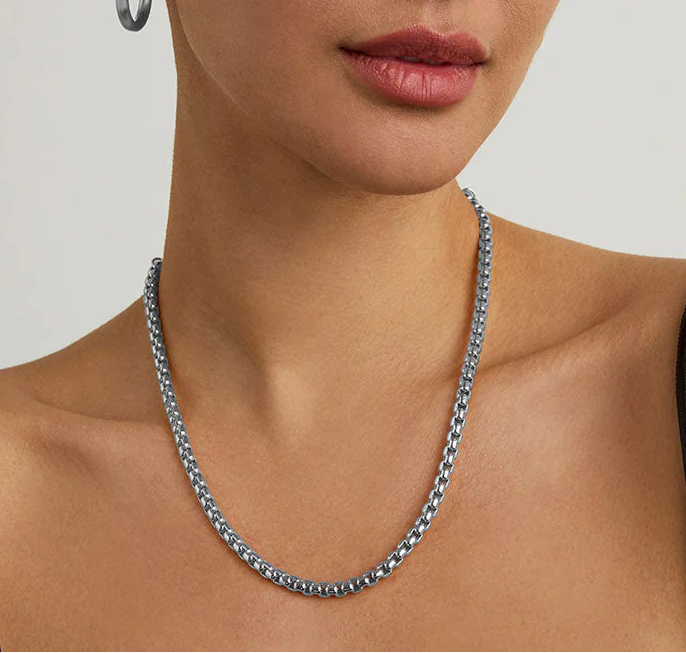 Woman wearing a silver chain necklace against a plain background