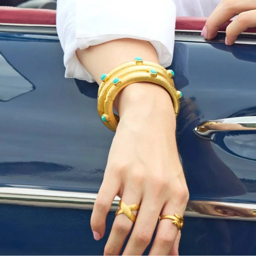 Woman wearing sunglasses and gold jewelry leaning on a classic car.
